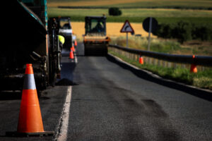 Construction zone on a roadway with orange traffic cones, paving machinery, and green fields in the background, illustrating asphalt paving work relevant to K&K Contracting's services.