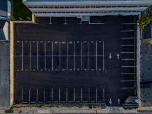 Aerial view of a freshly paved asphalt parking lot with clearly marked parking spaces and directional arrows, relevant to asphalt paving services and maintenance tips.