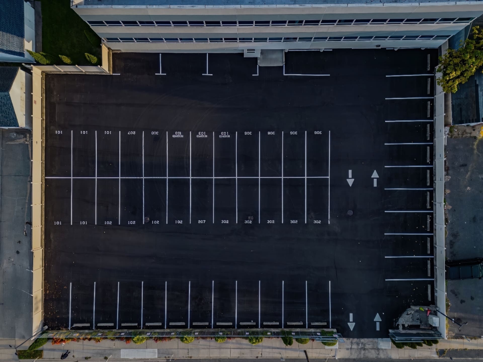 Aerial view of freshly paved asphalt parking lot with clearly marked spaces and directional arrows, showcasing K&K Contracting's paving services.