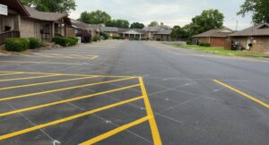 Freshly paved parking lot with newly painted yellow striping and marked spaces in a residential or office complex setting.