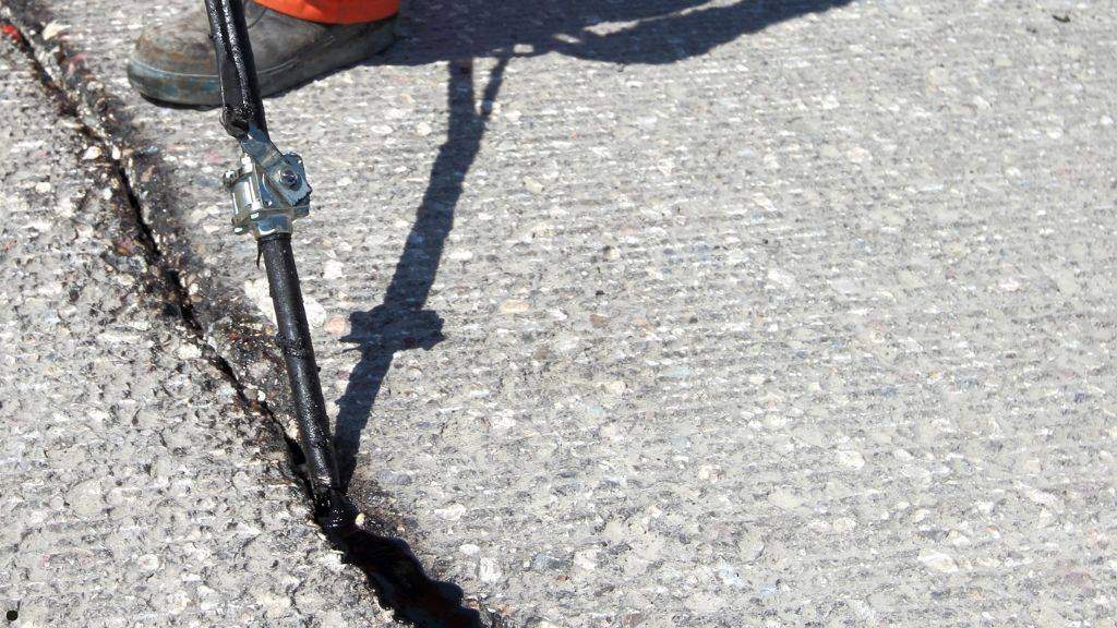 Maintenance worker applying hot rubberized crack filler to pavement cracks during fall commercial asphalt repairs
